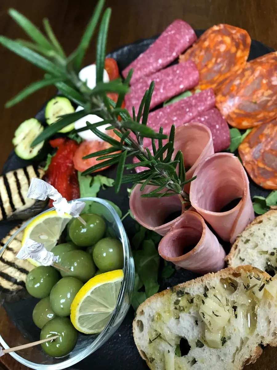 Nahaufnahme: Salami, Schinkenröllchen, Oliven, Zitrone und Knoblauchbrot