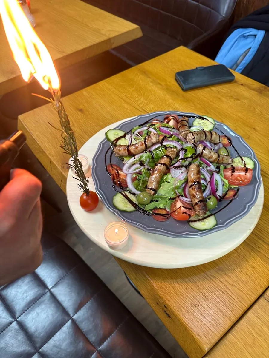 Salat mit Salsiccia, Gurke und Tomaten, daneben ein brennender Rosmarinzweig