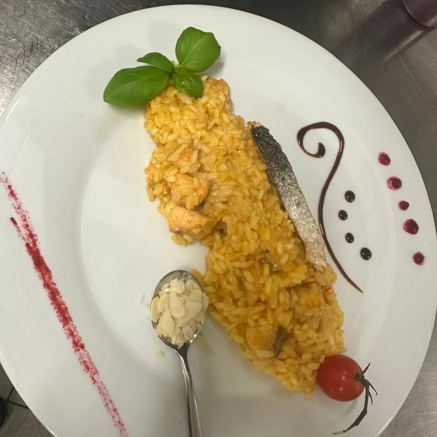 Lachsrisotto auf weißem Teller mit Basilikum und Tomate